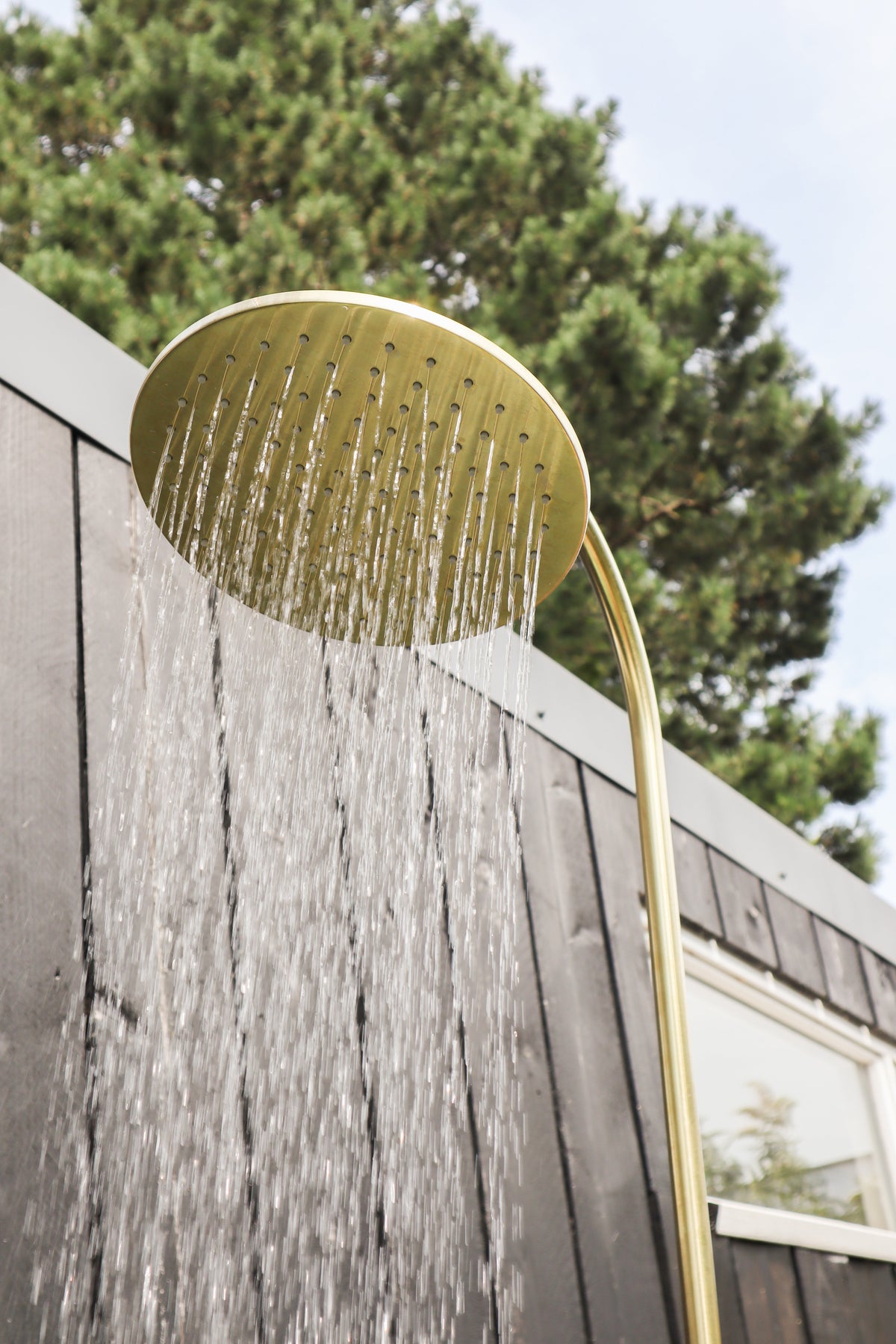 Brass Gardentub Shower with running water against a dark timber wall